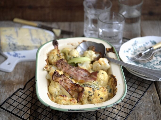 Blumenkohlgratin mit Blauschimmelkaese und gerösteten Speckstreifen, serviert in einer Auflaufform auf einem Rost auf einem gedeckten Holztisch.  | © StockFood / TT News Agency / TT News Agency