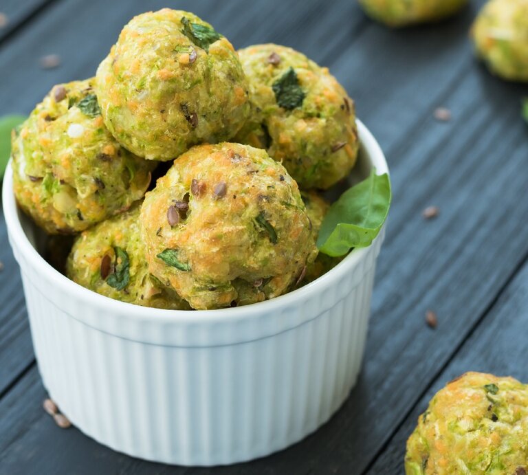 Ein paar Zucchini-Kugeln in einer kleinen weißen Schale auf einem schwarzen Holztisch. | © Shutterstock/ Vladyslav Rasulov
