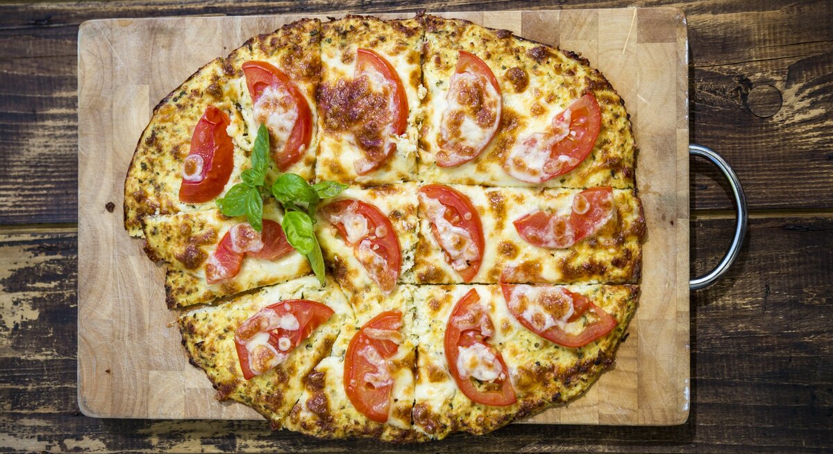 Mit Tomaten belegte Pizza auf Holzbrett, drapiert auf hölzernem Untergrund. 
