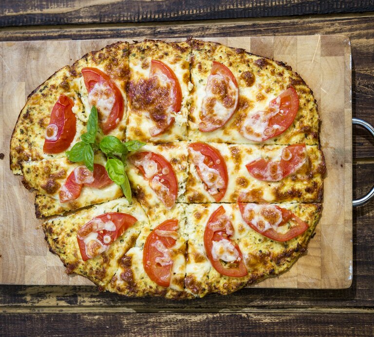 Mit Tomaten belegte Pizza auf Holzbrett, drapiert auf hölzernem Untergrund.  | © Getty Images/ Westend61