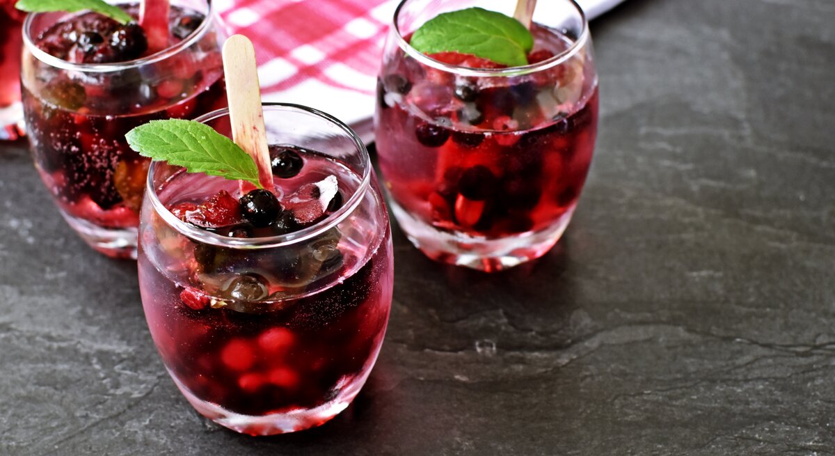 Drei Gläser mit Lillet Hot Berry auf einem grauen Steintisch.