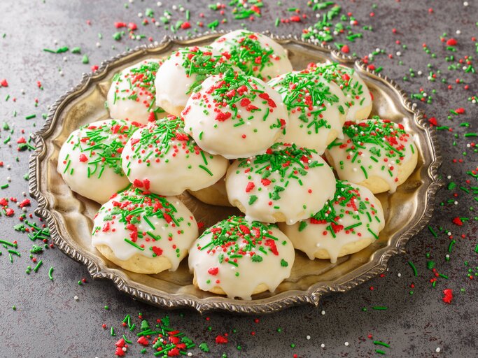 Runde Plätzchen mit Zuckerguss und bunten Streuseln auf Teller.  | © Getty Images/ALLEKO