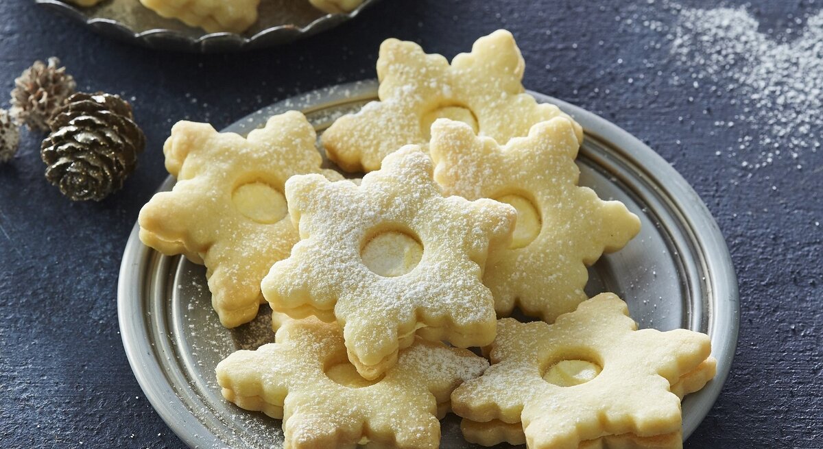 Auf einem Teller liegen Weihnachtsplätzchen mit Egg-Nogg-Creme. Sie sind mit Puderzucker bestreut.