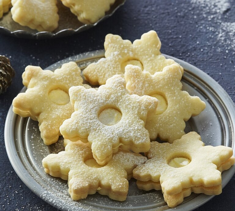 Auf einem Teller liegen Weihnachtsplätzchen mit Egg-Nogg-Creme. Sie sind mit Puderzucker bestreut. | © StockFood / [Profimedia]