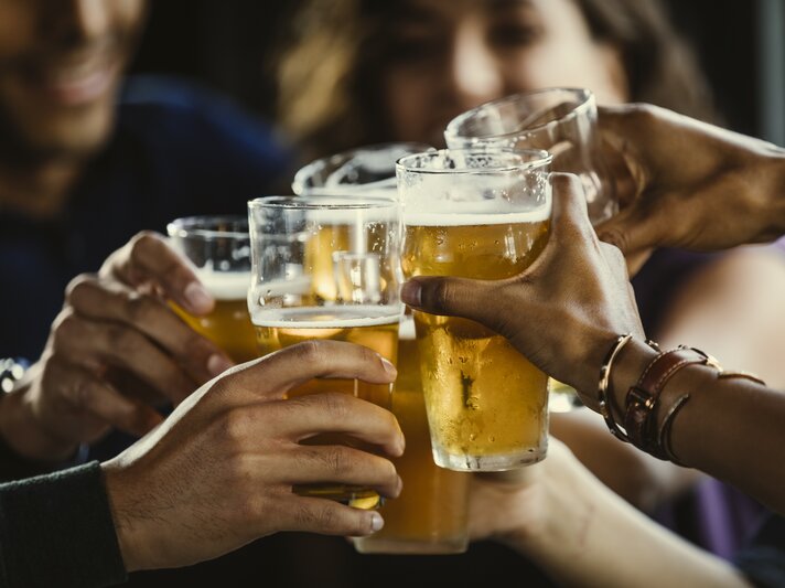 Junge Leute stoßen gemeinsam mit Bier an – in der Mitte sind die Gläser zu sehen | © Getty Images/The Good Brigade