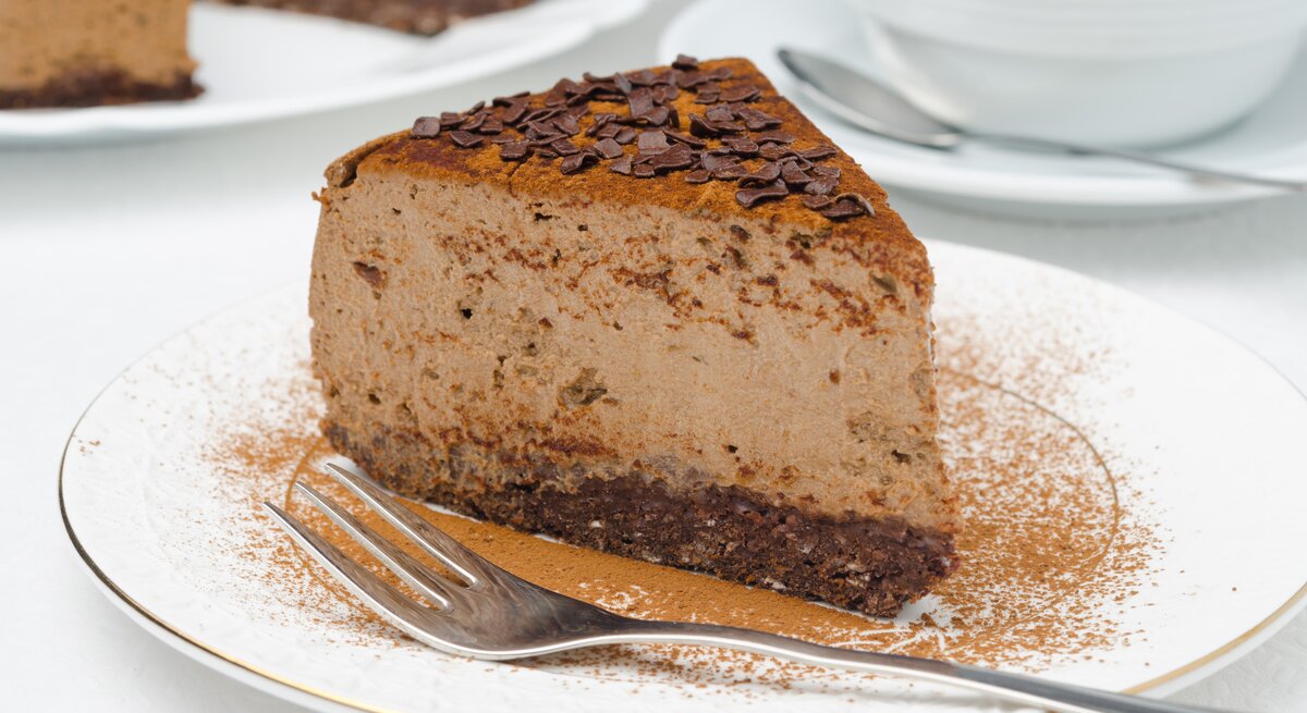 Ein Stück veganer Schokoladen-Cheesecake mit Kakao und Schokosplittern bestreut auf einem kleinen Teller.