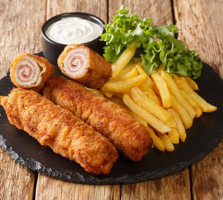 Flamenquín mit Pommes, Salat und Mayonnaise auf Schieferplatte, positioniert auf hölzernem Untergrund.  | © Getty Images/ALLEKO