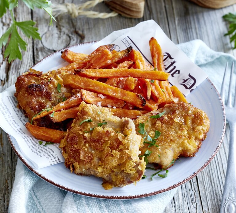 Crisp-Schnitzel mit Süßkartoffelpommes auf einem Teller. Rechts eine Gabel, links davon Petersilie. Draufsicht. | © EAT CLUB/ Isabell Triemer