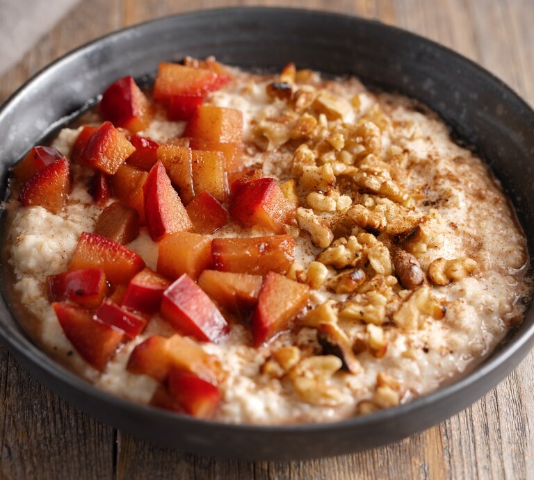 Eine schwarze Schüssel mit Walnuss-Pflaumen-Porridge auf einem Holztisch. | © GettyImages/nerudol