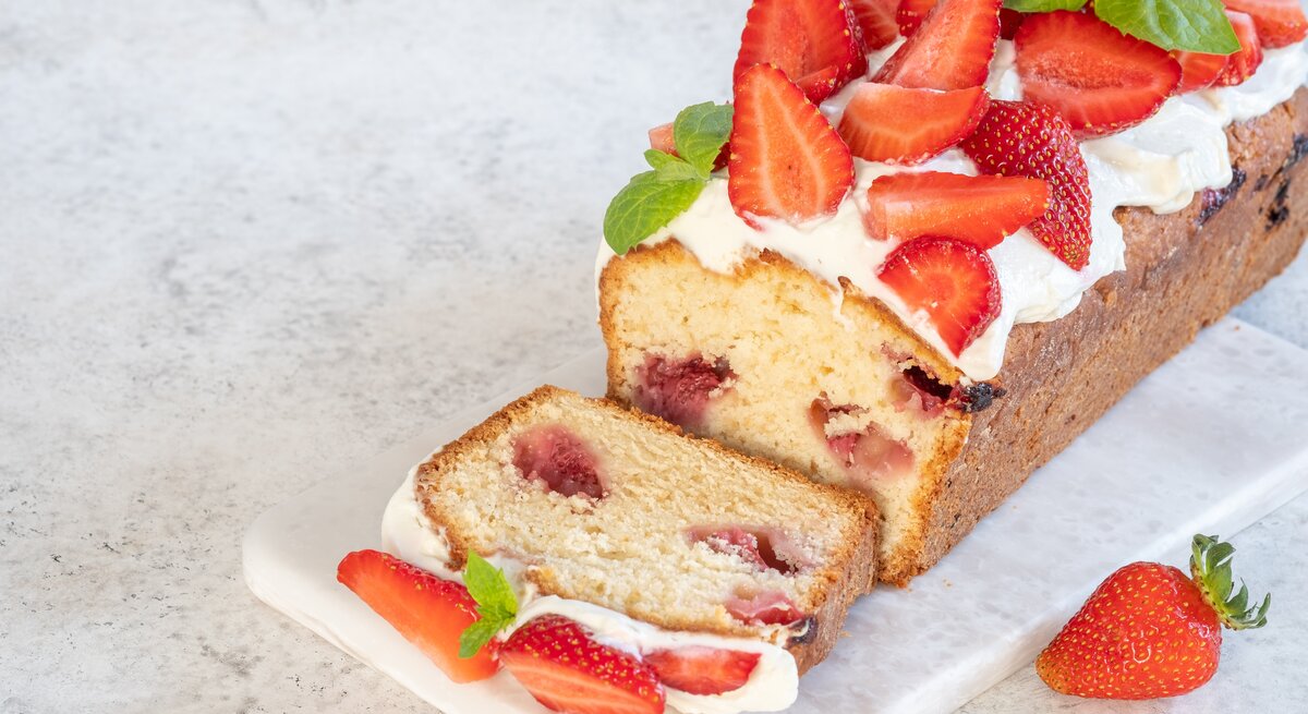 Erdbeer-Zitronenkuchen garniert mit frischen Erdbeeren auf hellem Untergrund. 