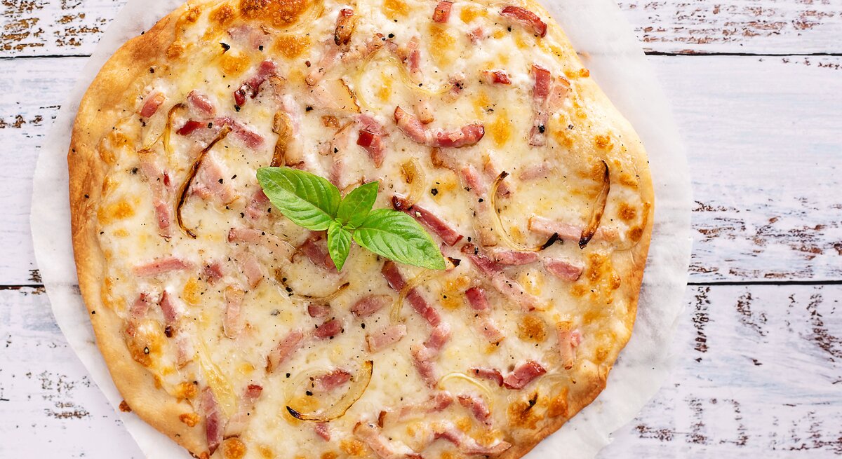 Carbonara-Pizza auf hellem, hölzernem Untergrund. 