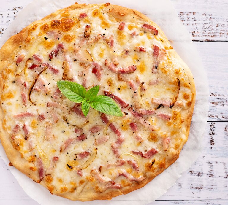 Carbonara-Pizza auf hellem, hölzernem Untergrund.  | © Getty Images/Cris Cantón