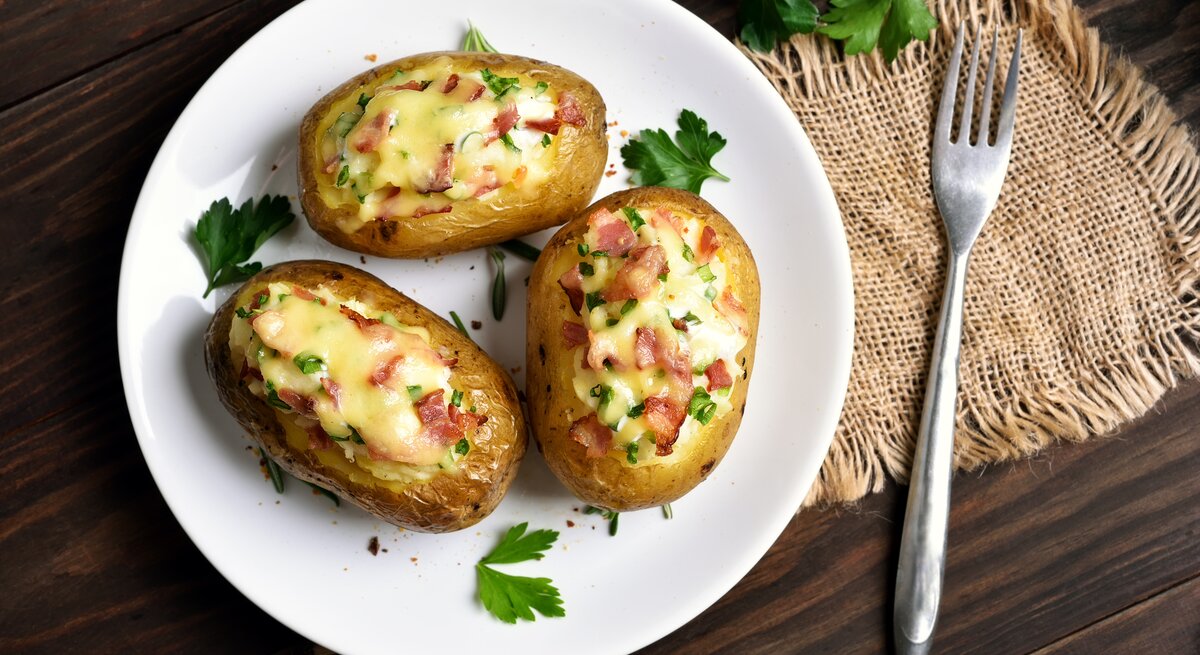 Gefüllte Kartoffeln mit Speck und Käse auf weißem Teller, angerichtet auf Holzuntergrund.