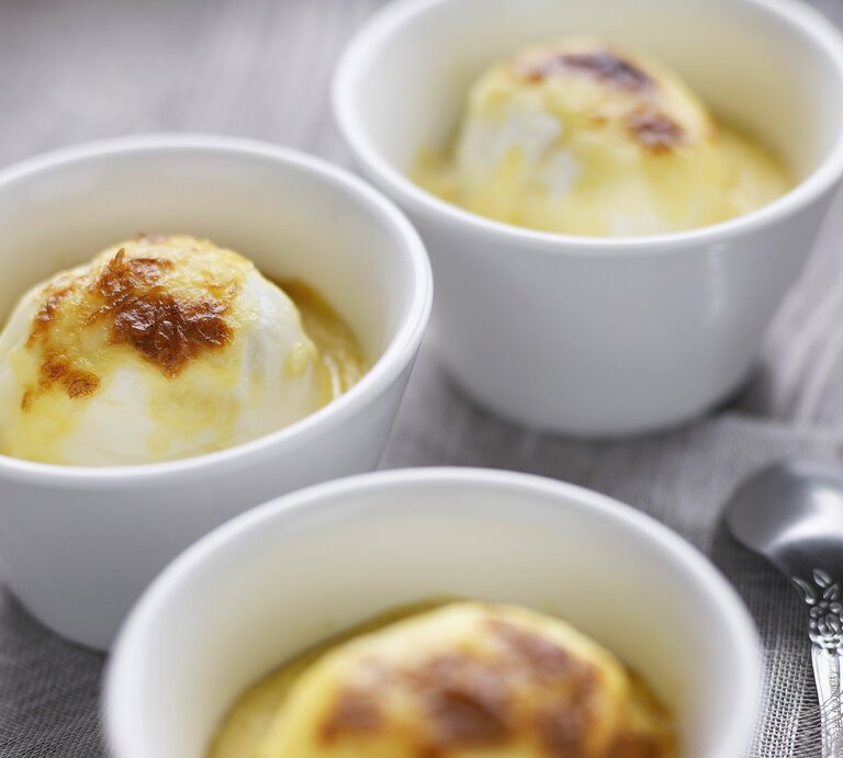 In weißen Förmchen überbackene Eier mit Bechamel, knusprig gratiniert und serviert auf einem grauen Holztisch.  | © StockFood / PhotoCuisine / Amiel, Jean-Claude