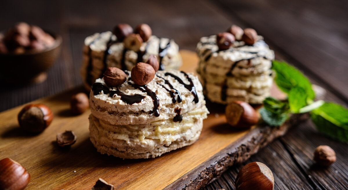 Haselnuss Baiser mit Creme auf einem Holzbrett mit Nüssen, Minze und Schokolade verziert.