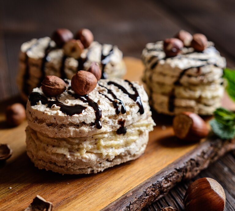 Haselnuss Baiser mit Creme auf einem Holzbrett mit Nüssen, Minze und Schokolade verziert. | © Gettyimages/ NoirChocolate