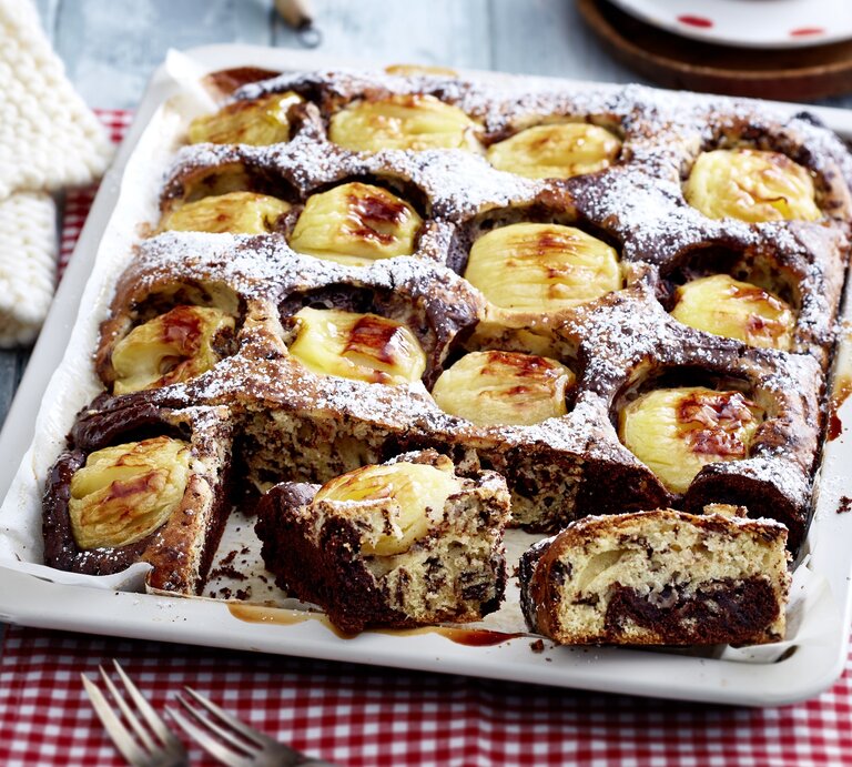 Ein Apfel-Stracciatella-Kuchen mit Gelee und Puderzucker in einem tiefen Blech. Der Kuchen ist angeschnitten und zwei Stücken liegen am Rand der Form. | © EAT CLUB/Isabell Triemer