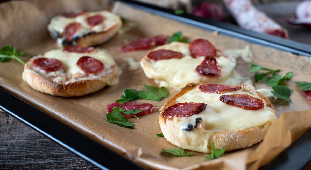 Ein mit Backpapier belegtes Blech mit Salami-Schmandbrötchen.
