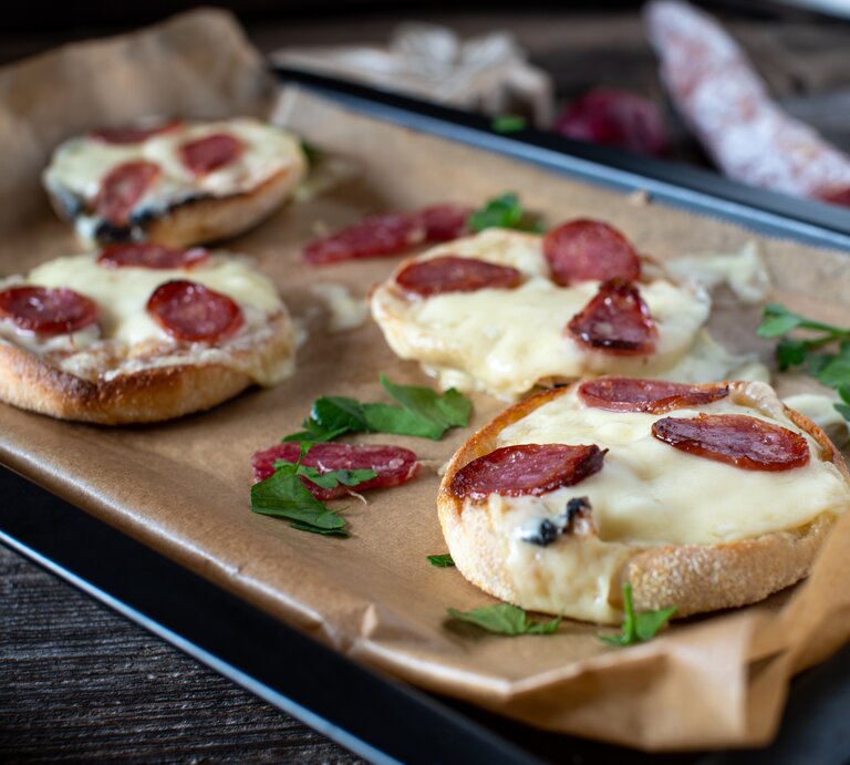 Ein mit Backpapier belegtes Blech mit Salami-Schmandbrötchen. | © GettyImages/Angelika  Heine
