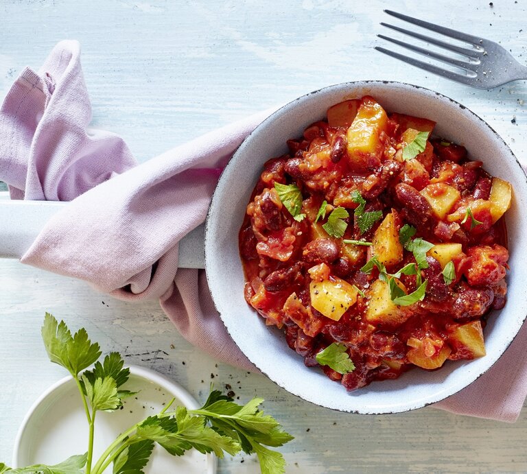 Kartoffel-Bohnen-Pfanne auf einem weißen Teller. Das Ganze auf einem blauen Untergrund.  | © EAT CLUB/ Isabell Triemer 
