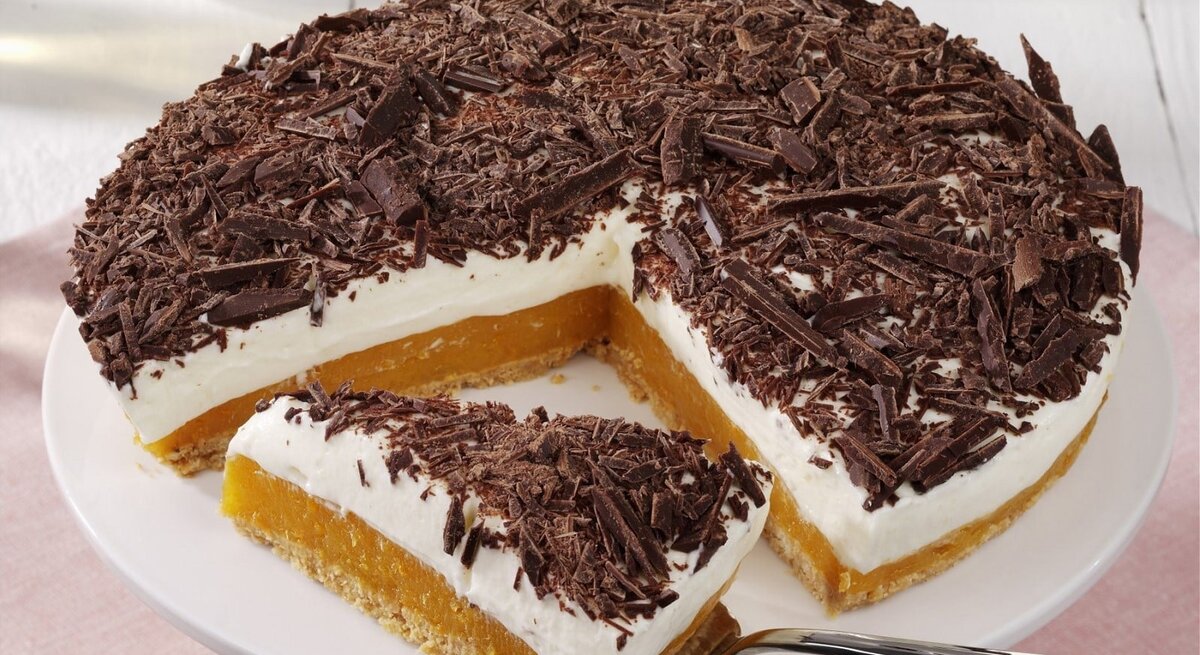 Auf einem Teller liegt eine Aprikosen-Joghurt-Torte ohne Backen. Sie ist mit Schokoraspeln bestreut.