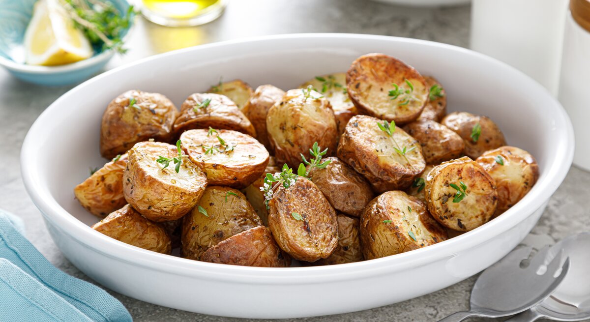 Eine weiße Schüssel mit gebackenen Kartoffeln und Thymian. 
