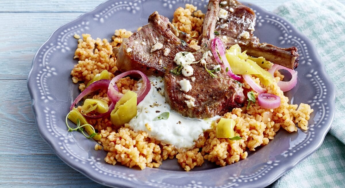 Griechische Koteletts vom Lamm auf Bulgur auf einem schön verzierten Teller der auf einem Untergrund aus Holz steht.