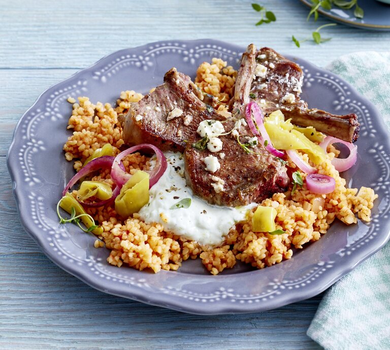 Griechische Koteletts vom Lamm auf Bulgur auf einem schön verzierten Teller der auf einem Untergrund aus Holz steht. | © EAT CLUB/Isabell Triemer