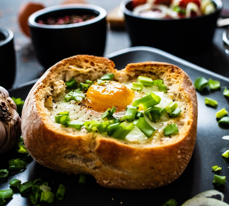Eier im Brötchen gebacken auf einem dunklen Teller. Daneben verschiedene Schalen mit verschiedenen Zutaten.  | © Shutterstock /Jacek Chabraszewski