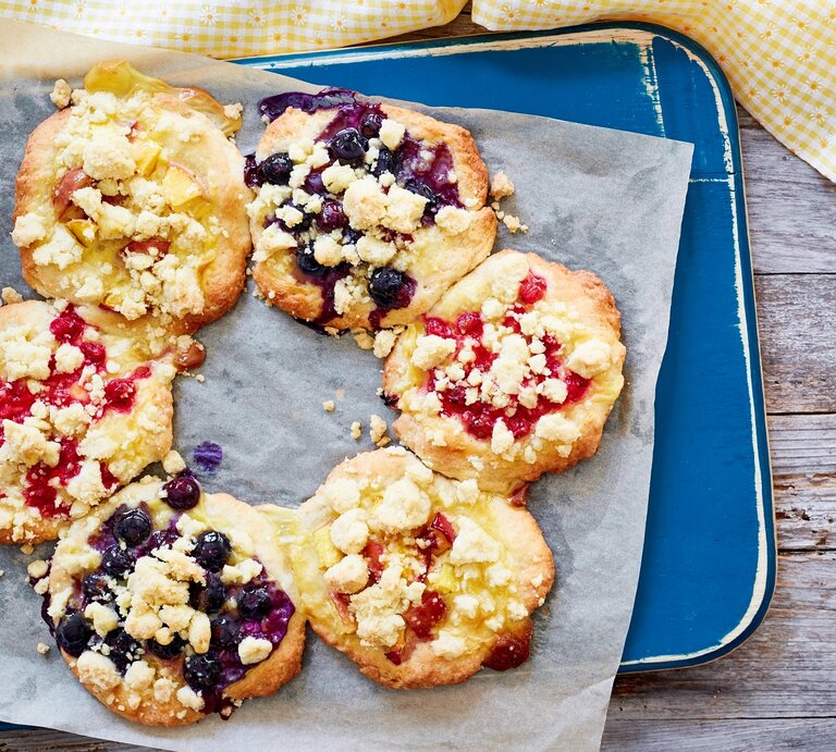 Streuseltaler-Kranz mit fruchtigen Beeren und Vanillepudding, serviert auf einem hellblauen Tablett auf einem groben Holztisch. | © EAT CLUB / Isabell Triemer