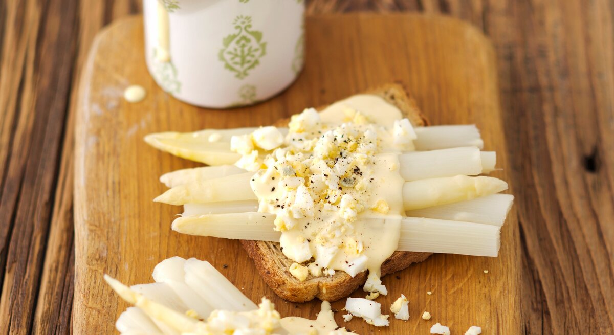 Toast mit Spargel und Eier-Soße auf Holzbrett serviert.