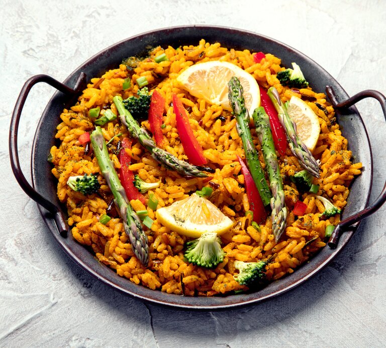 Eine vegane Paella mit grünem Spargel, Zitronenscheiben, Paprika und Brokkoli in einer typischen Paella-Pfanne. | © Getty Images/bit245