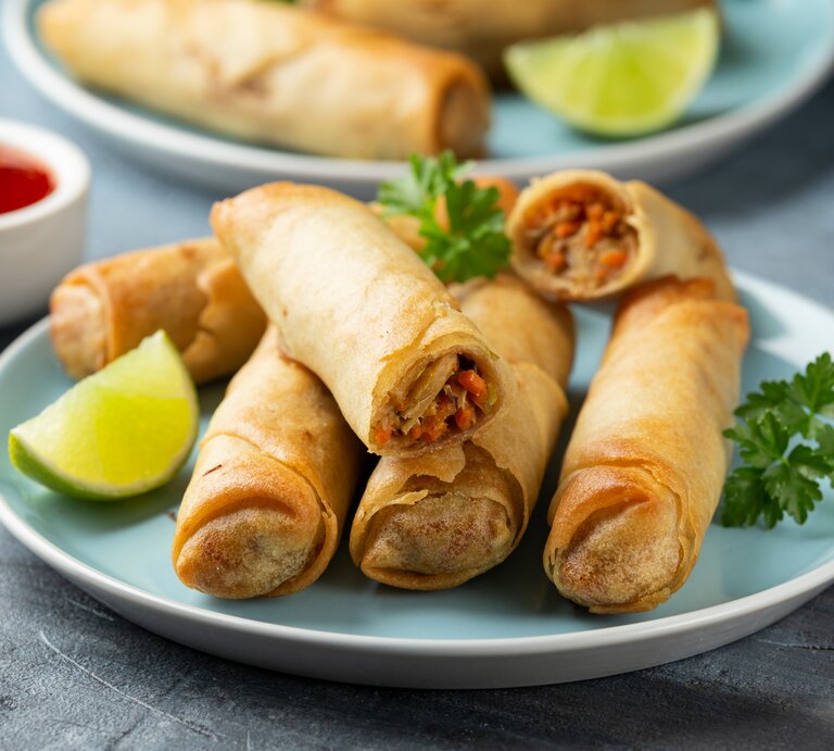 Auf zwei blauen Tellern liegen vegane Frühlingsrollen, dazwischen steht eine weiße Schale mit roter Soße zum Dippen. | © Getty Images/ DronG