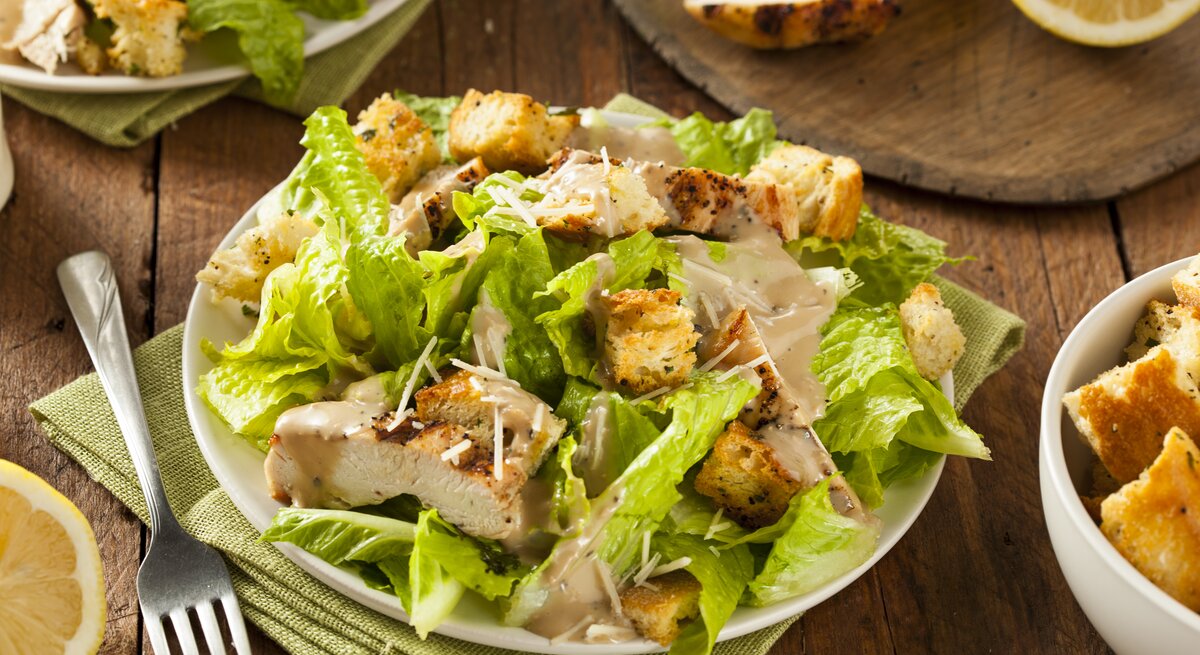 Caesar Salad mit gegrillter Putenbrust und Salatblättern / runder Teller / Gabel / Stoffserviette / angeschnittene Zitrone / Draufsicht, schräg
