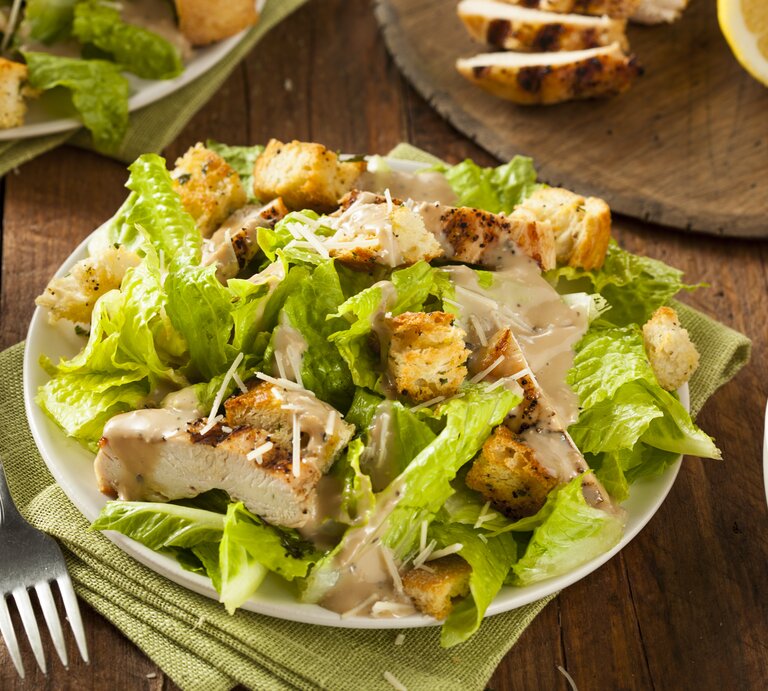 Caesar Salad mit gegrillter Putenbrust und Salatblättern / runder Teller / Gabel / Stoffserviette / angeschnittene Zitrone / Draufsicht, schräg | © istock/bhofack2 