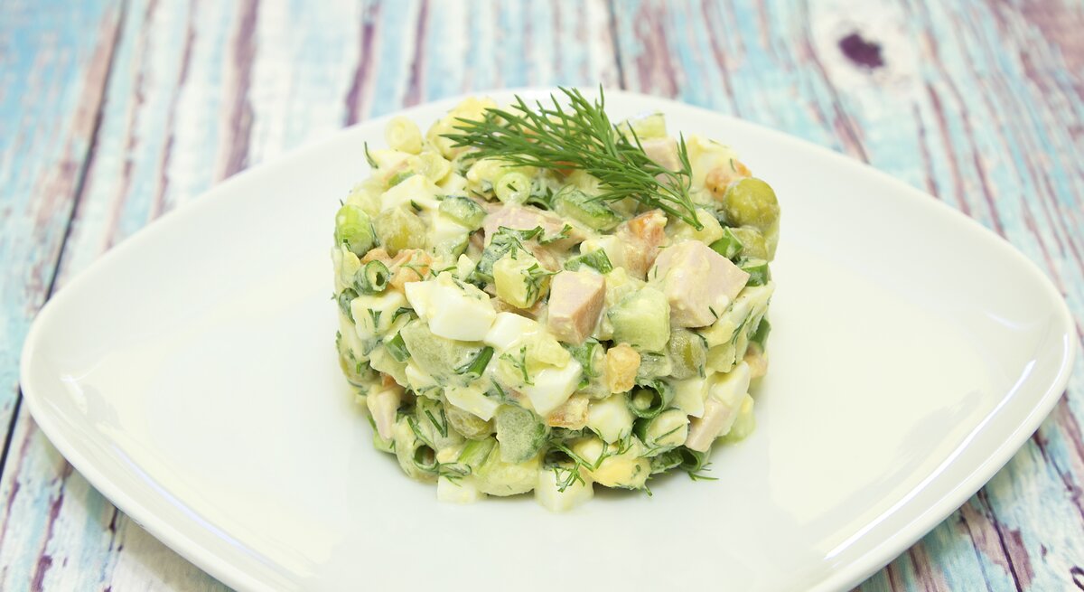 Ein Teller mit persischem Kartoffelsalat, auch Sālād Olivieh genannt, auf einem bunten Holztisch.