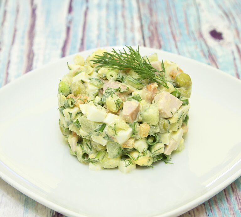 Ein Teller mit persischem Kartoffelsalat, auch Sālād Olivieh genannt, auf einem bunten Holztisch. | © Getty Images/ tasha_lyubina
