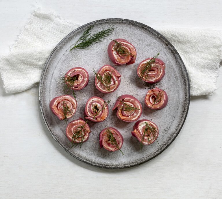 Rote-Bete-Pfannkuchenröllchen mit Lachs und Meerrettich, gerollt und in kleine Happen geschnitten serviert auf einem grauen Tisch auf einem weißen Tisch. | © StockFood / Cawley, Julia