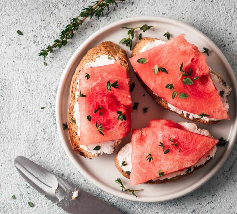 Ein Teller mit Brotscheiben, auf denen Frischkäse und veganer Thunfisch aus Wassermelone liegt. Bestreut mit frischen Kräutern. Draufsicht. | © Getty Images/ Fascinadora
