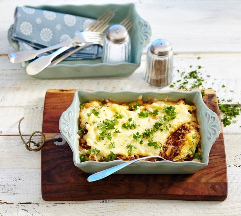 Eine Auflaufform mit Polenta-Hackfleischgratin. Daneben weiteres Besteck und Geschirr und Salz und Pfeffer. Das Ganze auf einem hölzernen Untergrund.  | © StockFood / Teubner Foodfoto