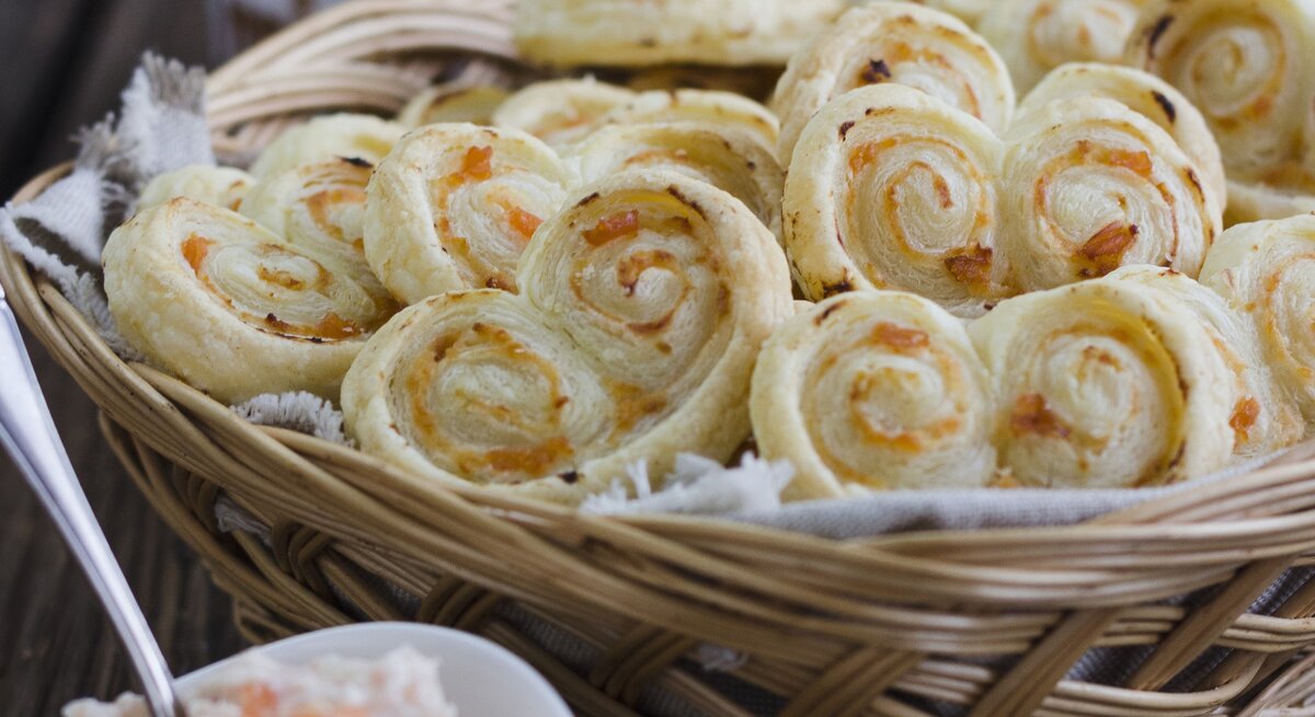 Blätterteigschnecken mit Lachs und Meerettich-Frischkäse, gestapelt in einem großen Korb, serviert mit der Lachs-Creme auf einem hölzernen Tisch. 