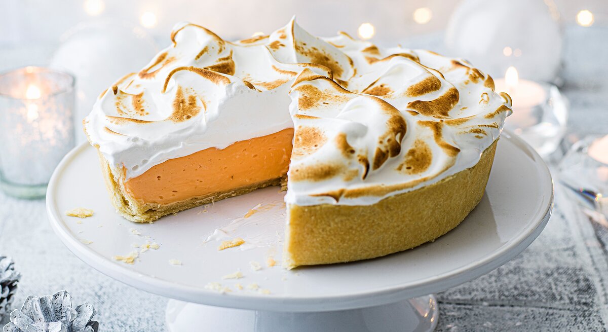 Ein angeschnittener Negroni-Pie mit goldbraun gebräuntem Baiser steht auf einer weißen Tortenplatte.