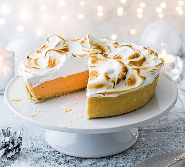 Ein angeschnittener Negroni-Pie mit goldbraun gebräuntem Baiser steht auf einer weißen Tortenplatte. | © StockFood / Immediate Media / Olive