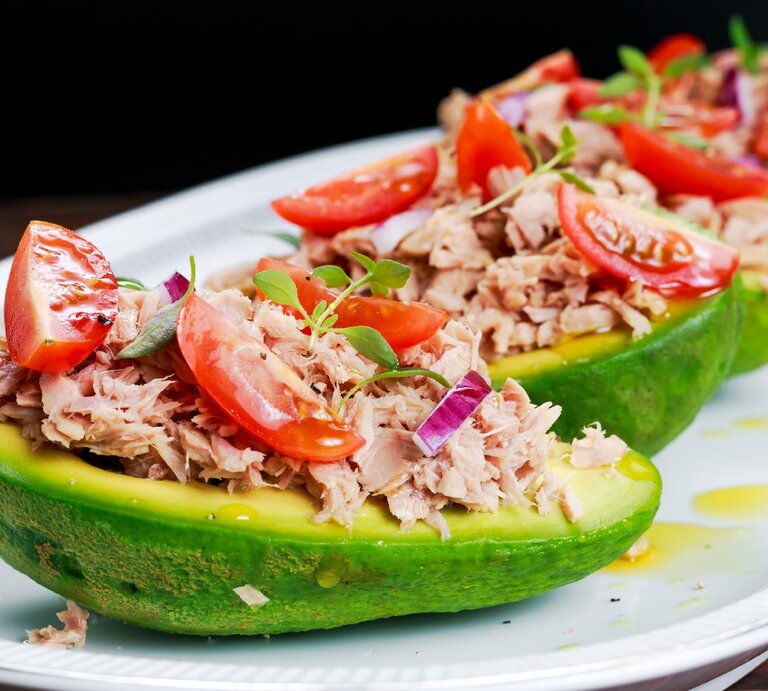 Ein weißer länglicher Teller mit vier Avocadohälften, in denen der Thunfischsalat angerichtet ist vor schwarzem Hintergrund. | © Shuuterstock/ DronG