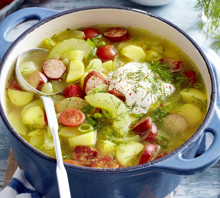 In einem Topf ist eine Portion Schmorgurken-Kabanossi-Eintopf angerichtet. Sie ist mit Dill und saurer Sauce serviert.  | © EAT CLUB / Isabell Triemer