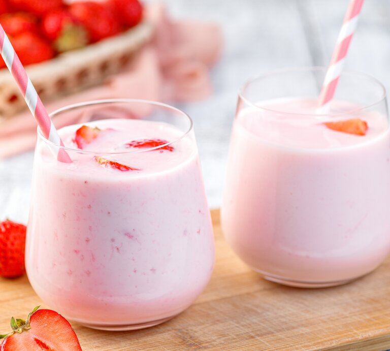 Zwei Gläser mit Erdbeermilchshake und gestreiftem Strohhalm stehen auf einem Holzbrett. Daneben liegen Erdbeeren.  | © Getty Images/Dmitrii Ivanov