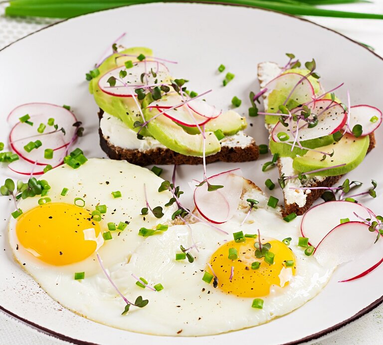 Ein weißer Teller mit kleinem schwarzen Rand und dem belegten Pumpernickel von der Seite fotografiert auf einem weißen Tisch.  | © Shutterstock/ Timolina