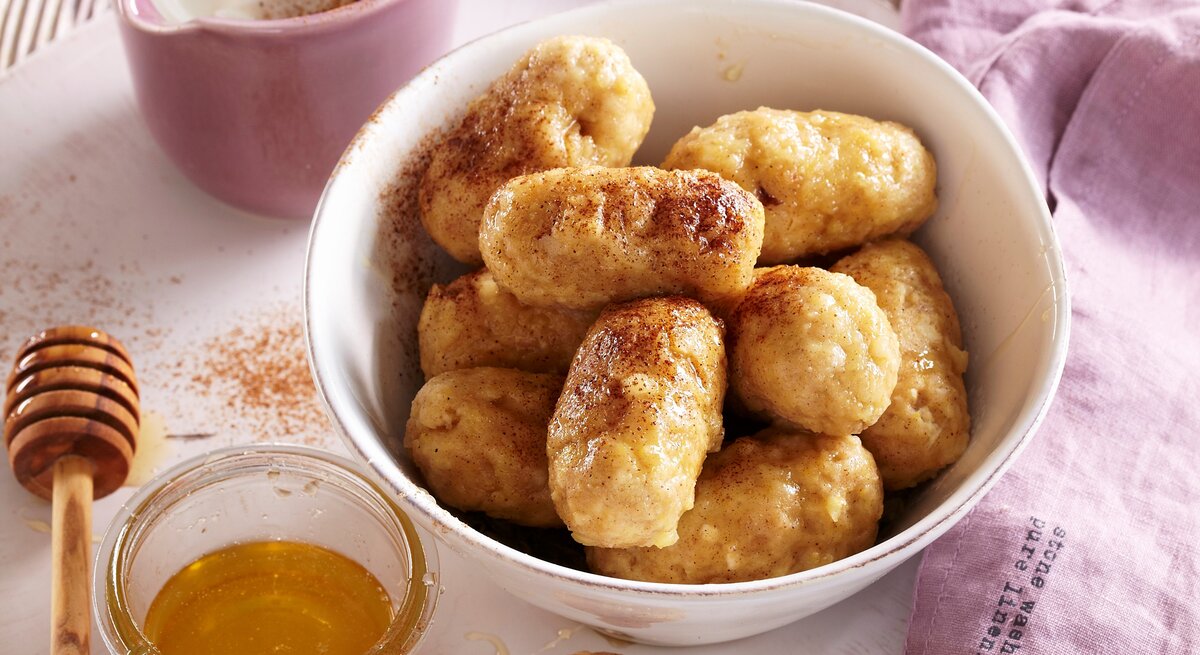 In einer weißen Schüssel liegen saftige Vanille-Apfel-Knödel. Sie sind mit Honig und Zimt verfeinert. 