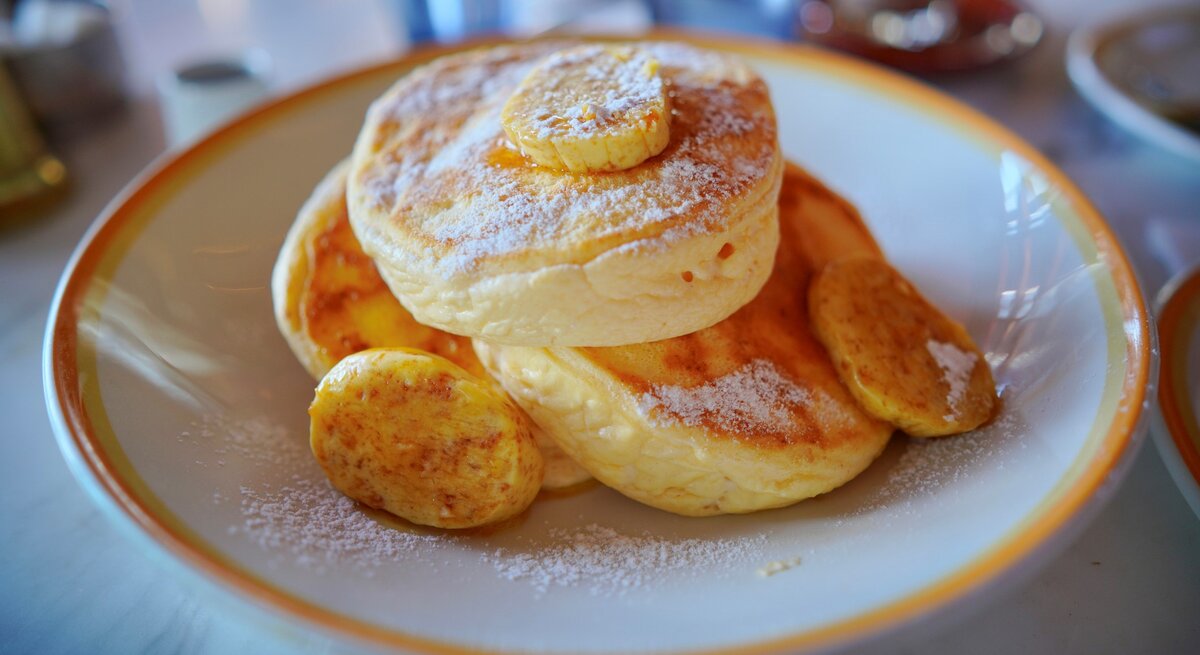 Drei japanische Pancakes mit einigen kartamellisierten Bananenscheiben in einem tiefen hellen Teller auf einem Marmoruntergrund.
