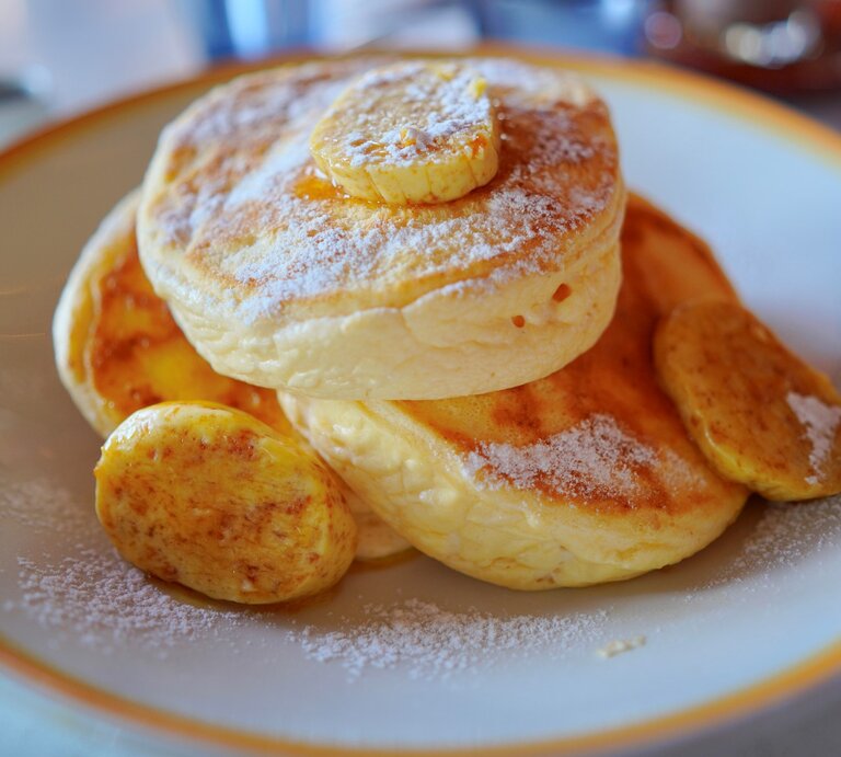 Drei japanische Pancakes mit einigen kartamellisierten Bananenscheiben in einem tiefen hellen Teller auf einem Marmoruntergrund. | © Gettyimages/ SkYGoN
